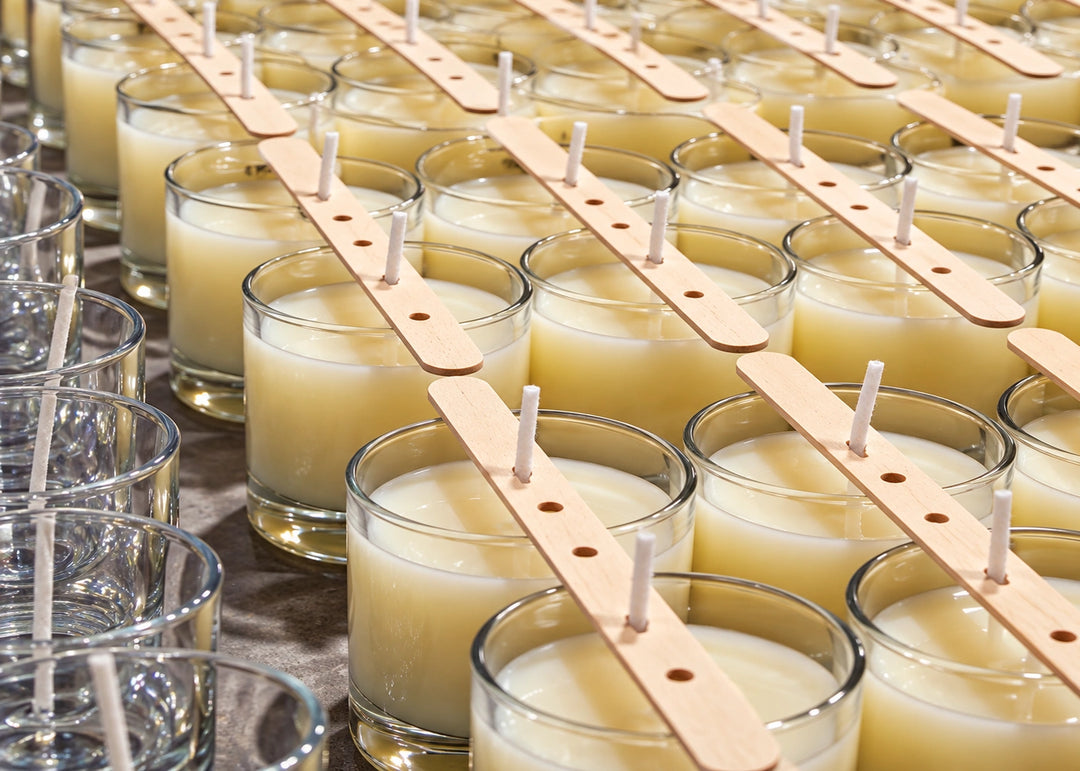 Vasos con cera recién vertida y centradores de pabilo alineados durante la producción