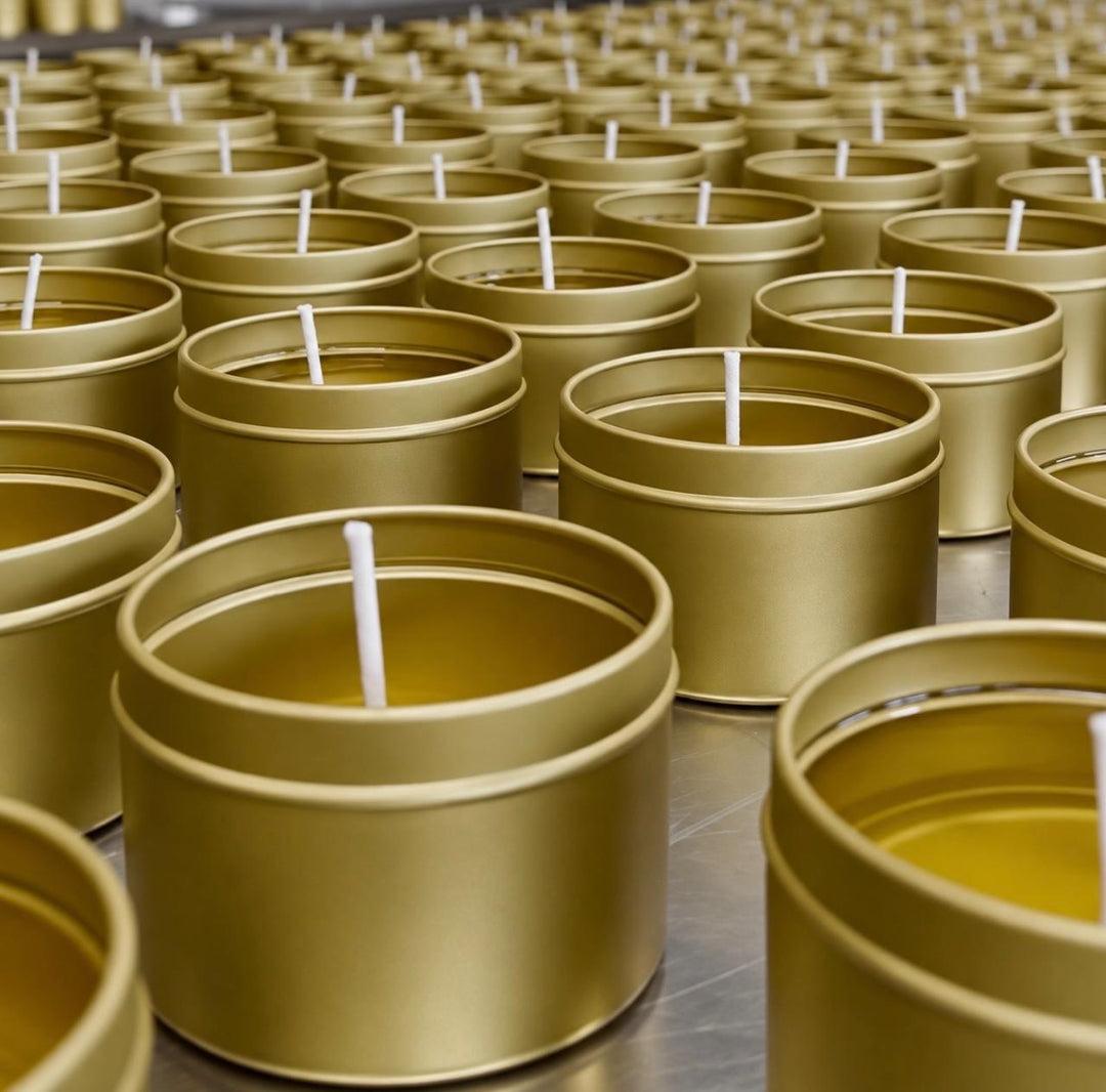 Latas doradas con cera recién vertida y pabilo, alineadas en el taller