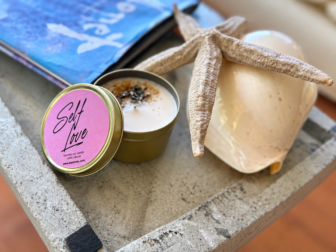 Vela Self Love de Alaïa en lata con tapa rosa, junto a una estrella de mar y una concha