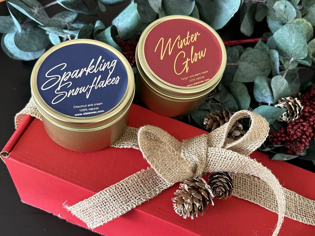 Latas doradas Sparkling Snowflakes y Winter Glow de Alaïa sobre una caja roja con moño de yute