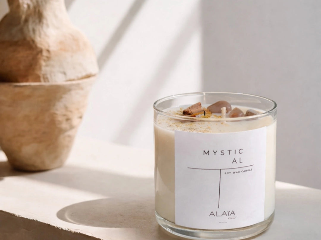 Vela Mystical de Alaïa en vaso transparente junto a un jarrón de barro